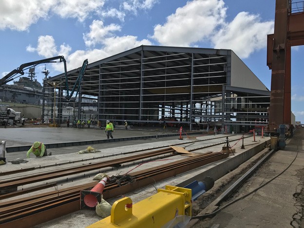 A U.S. naval ship is seen in the background as workers pour Penetron-treated concrete at a new building project at the General Dynamics NASSCO shipyard in San Diego